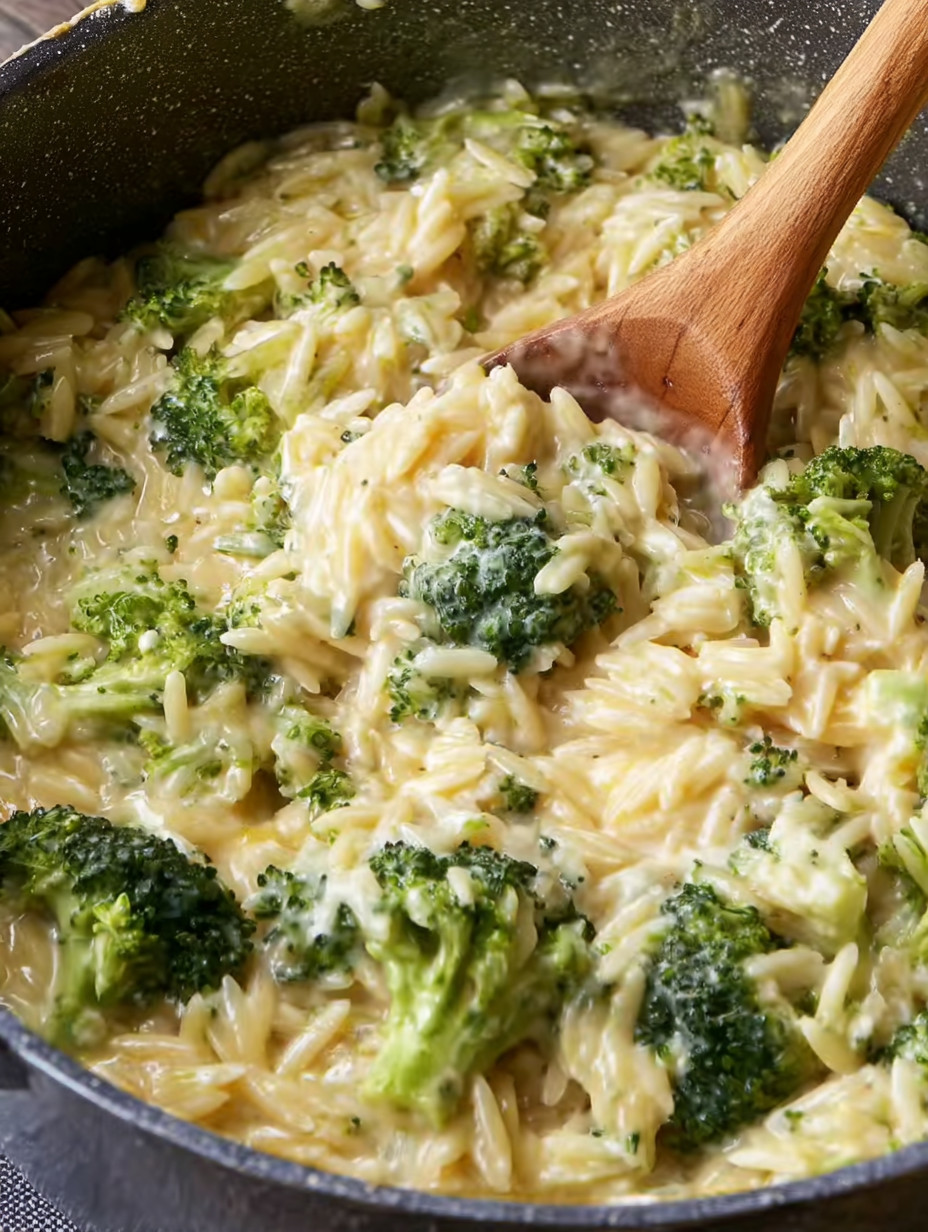 A wooden spoon is in a bowl of pasta and broccoli.
