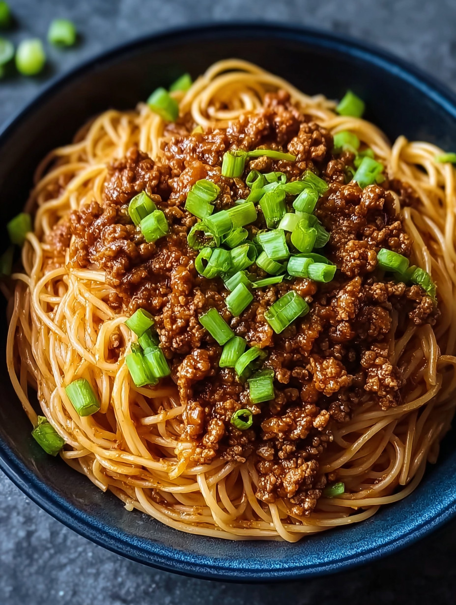 A bowl of spaghetti with meat sauce and green onions.