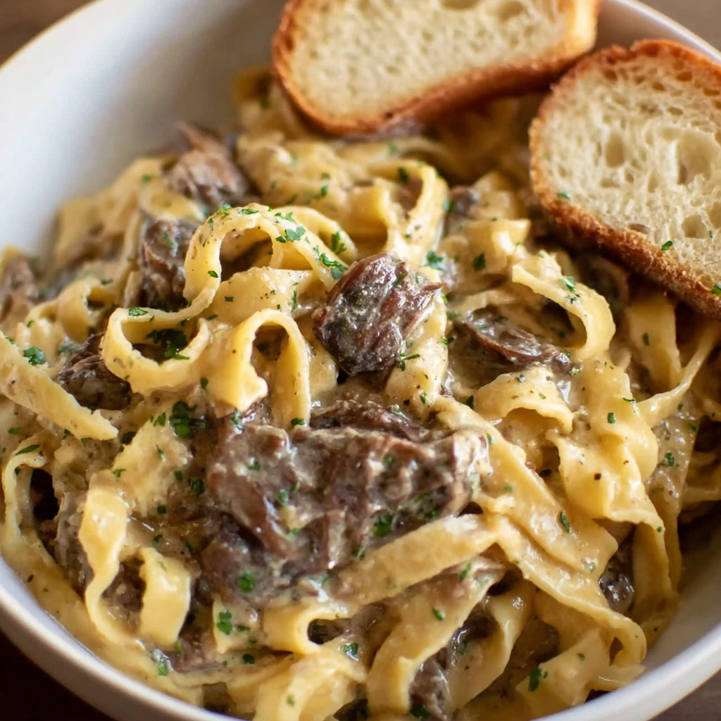 A bowl of pasta with meat and bread.