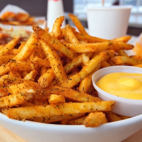 A bowl of fries with a cup of sauce.